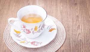 Tazza di tè caldo con foglie di tè e limone su tavolo di legno, ideale per bruciare grassi addominali.